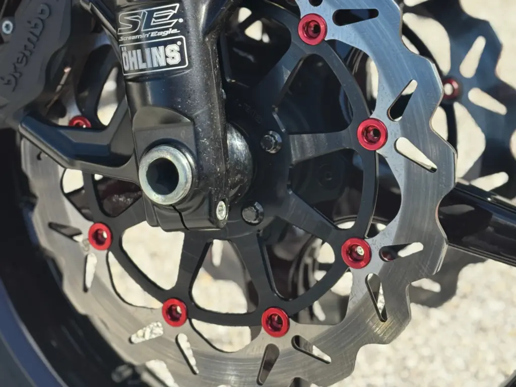 Close-up of a VTwin motorcycle brake rotor with performance hardware installed, featuring GBrakes rotor design and upgraded suspension components.